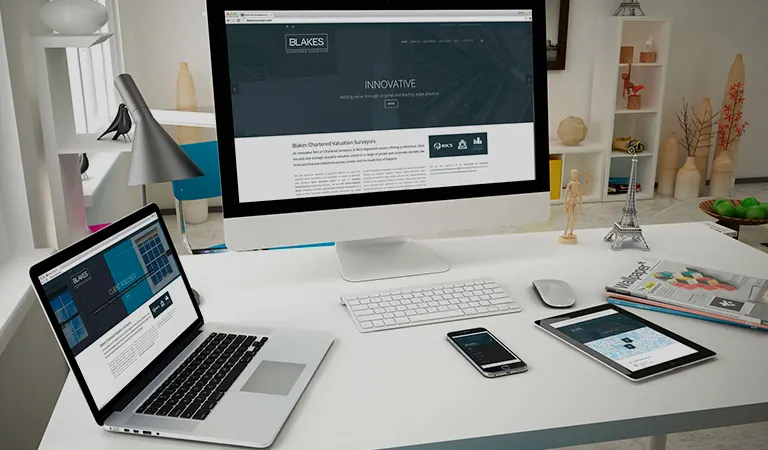 Mesa de trabalho com monitor, notebook e tablet exibindo um layout